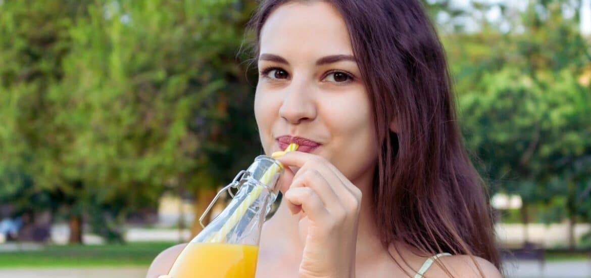 A woman sips an orange drink from a bottle with a straw