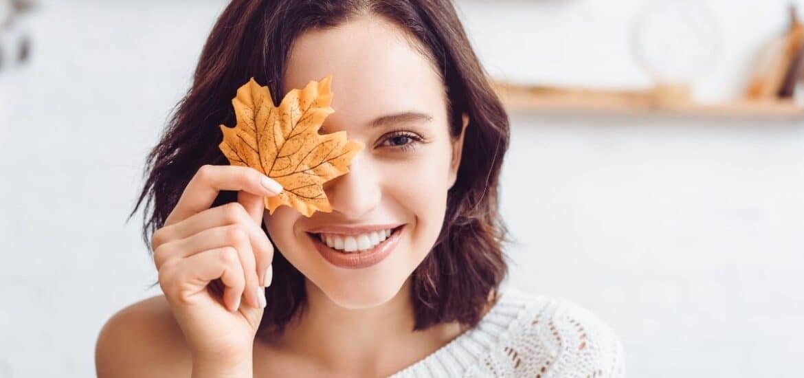 Woman with warm white smile holding a decorative autumn leaf